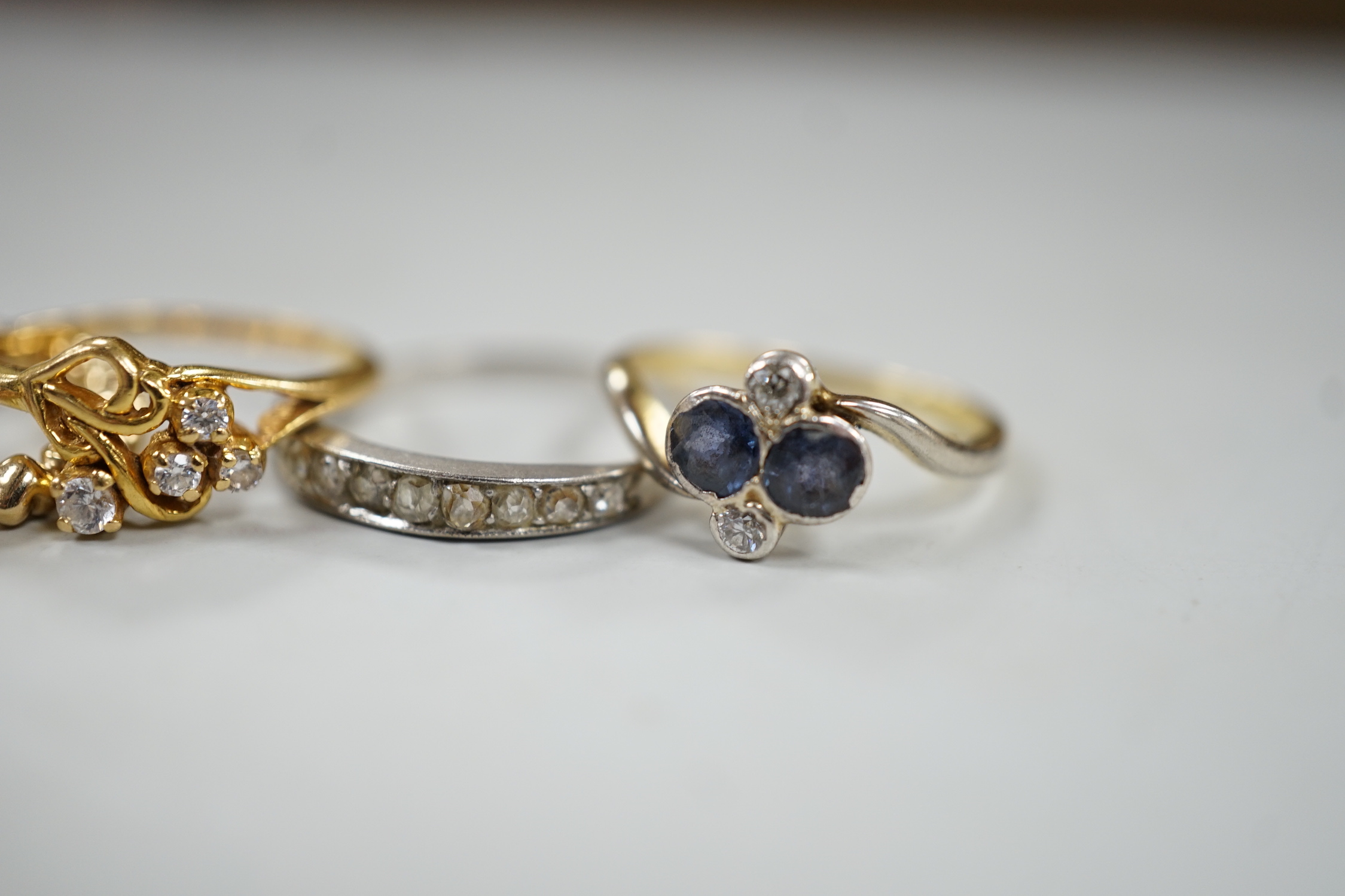 Three assorted white or yellow metal and gem set rings, including sapphire and diamond four stone cross over ring and a graduated diamond chip set half eternity ring, a similar three colour band, gross weight 8 grams and